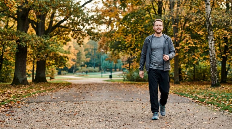 Man walking on a tree-lined park path in autumn as an everyday mental health exercise